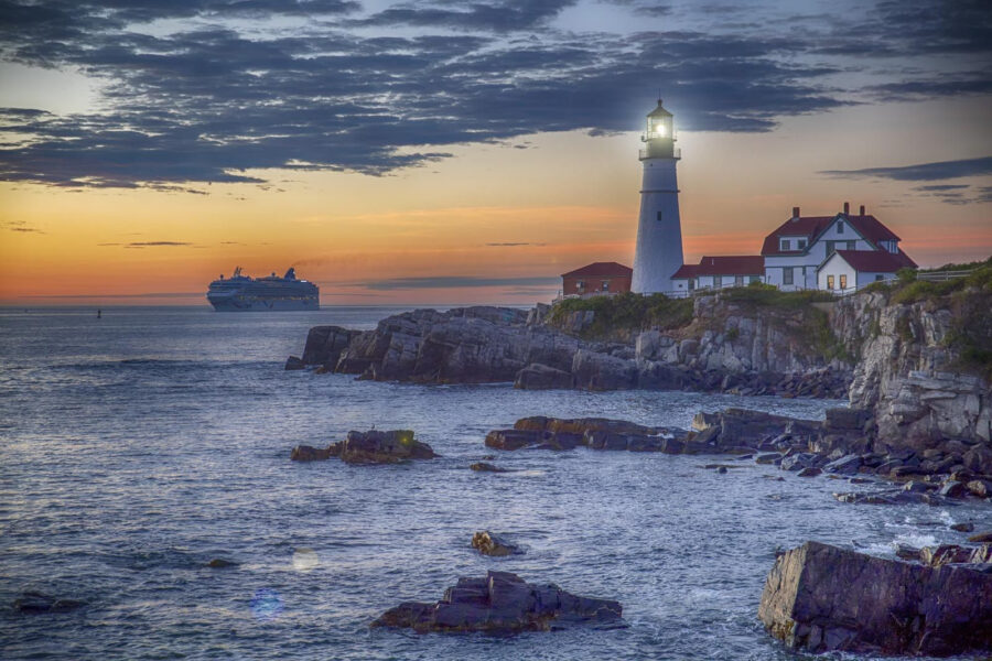 Lighthouse on a rocky shore with a cruise ship in the background