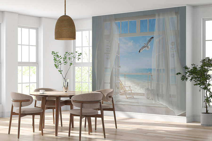 View of a beach from a room with a bird flying over it