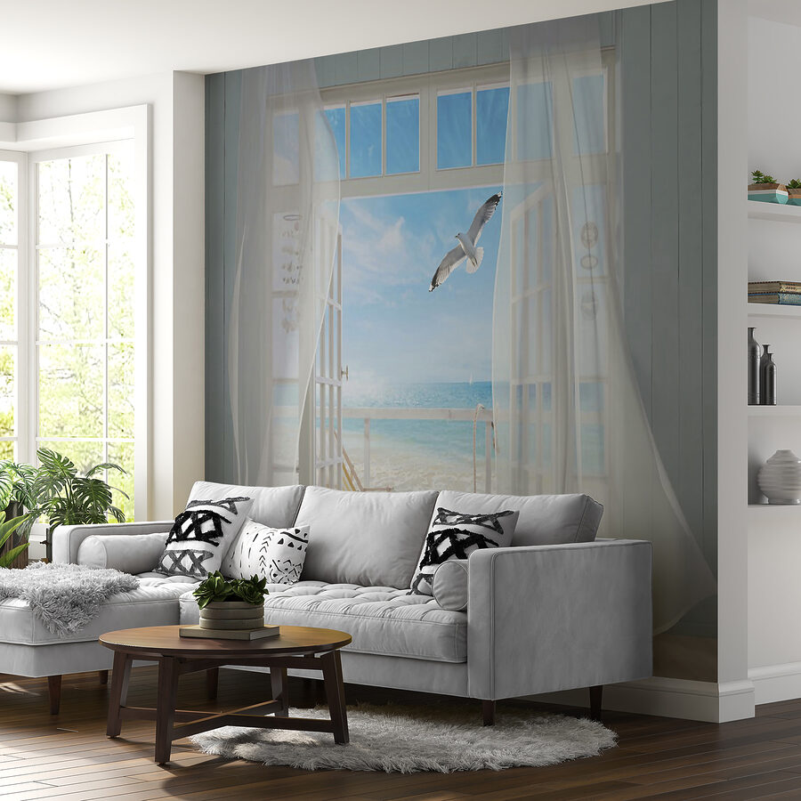 View of a beach from a room with a bird flying over it